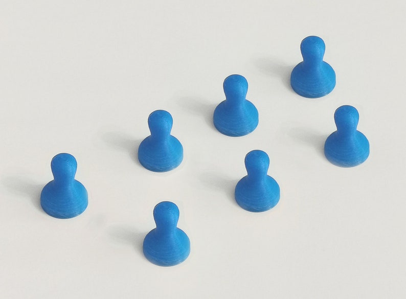 May include: Seven blue push pins arranged on a white surface. Each pin has a rounded top and a wider base, resembling a person-shaped design. The pins are evenly spaced, creating a visually appealing pattern.