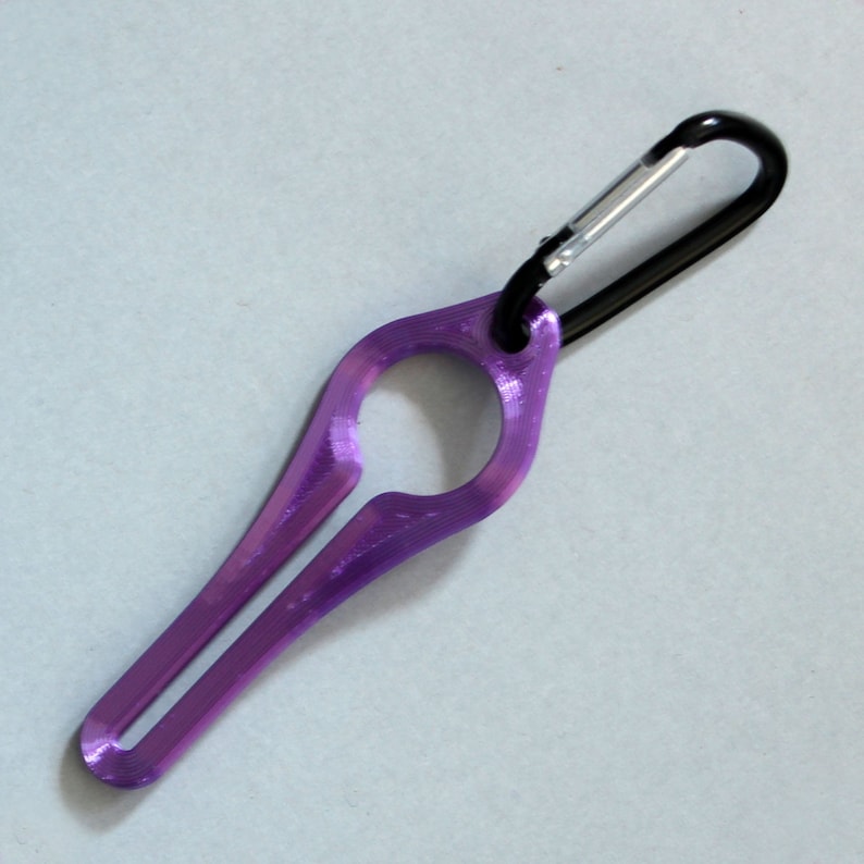 Puede incluir: Un llavero de pl&aacute;stico morado con un mosquet&oacute;n negro. El llavero tiene forma de anillo con un peque&ntilde;o agujero en el centro.