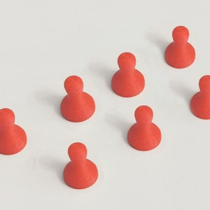May include: Seven red game pieces, each with a rounded base and a cylindrical top, are arranged on a white surface. The pieces are evenly spaced and appear to be made of a solid material.