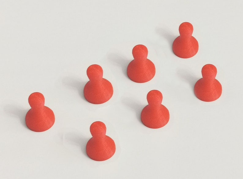 May include: Seven red game pieces, each with a rounded base and a cylindrical top, are arranged on a white surface. The pieces are evenly spaced and appear to be made of a solid material.
