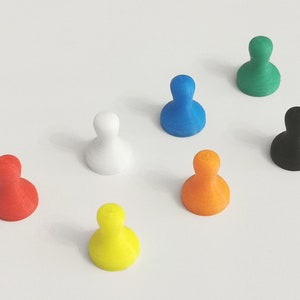 May include: An assortment of colorful push pins in red, white, yellow, orange, blue, green, and black. These small, rounded pins are arranged on a white surface, offering a vibrant display of office or craft supplies.