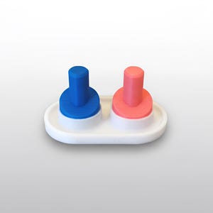 May include: A white, oval-shaped salt and pepper shaker set. The set features two cylindrical, colored tops: one blue and one coral. Each top sits on a matching, ribbed base. The set is designed for tabletop use.