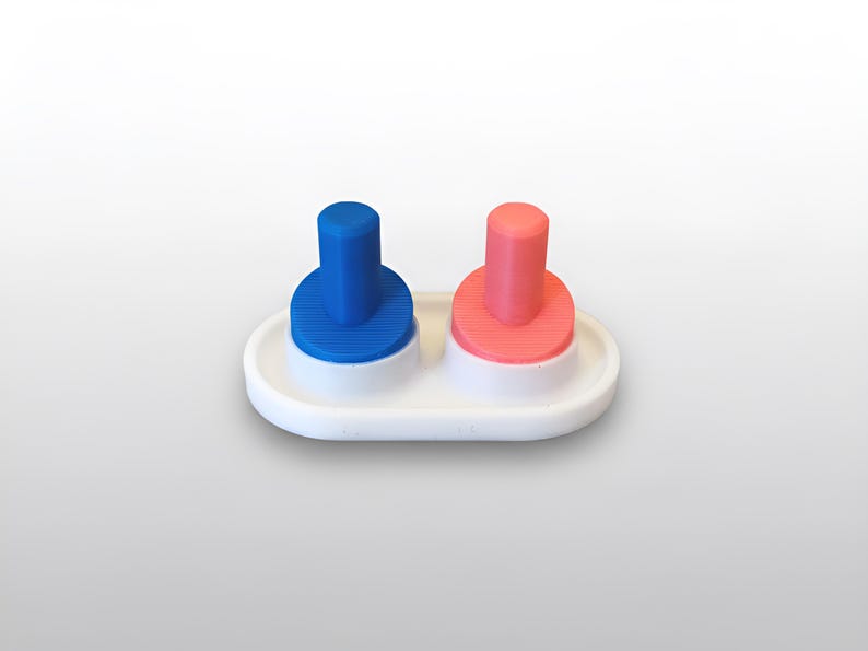 May include: A white, oval-shaped salt and pepper shaker set. The set features two cylindrical, colored tops: one blue and one coral. Each top sits on a matching, ribbed base. The set is designed for tabletop use.