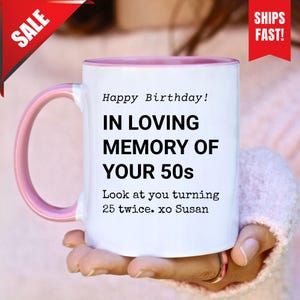 Peut inclure: Mug en céramique blanche avec intérieur et anse roses. Le mug affiche le texte "Happy Birthday! IN LOVING MEMORY OF YOUR 50s" et "Look at you turning 25 twice. xo Susan". Une bannière rouge "SALE" est en haut à gauche.