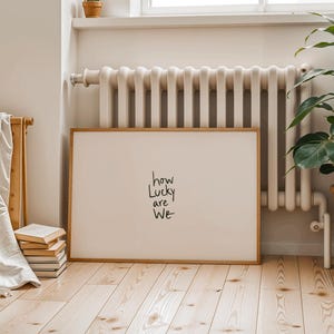 A minimalist wall art print featuring the quote “How Lucky Are We” in elegant hand-drawn typography on a neutral background. The modern canvas design exudes warmth and simplicity, perfect for couples who value love and gratitude. This inspirational quote poster adds a timeless touch to any contemporary or boho-style home. A beautifully crafted neutral wall decor piece that symbolizes appreciation, connection, and modern elegance.