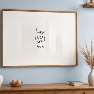A minimalist wall art print featuring the quote “How Lucky Are We” in elegant hand-drawn typography on a neutral background. The modern canvas design exudes warmth and simplicity, perfect for couples who value love and gratitude. This inspirational quote poster adds a timeless touch to any contemporary or boho-style home. A beautifully crafted neutral wall decor piece that symbolizes appreciation, connection, and modern elegance.