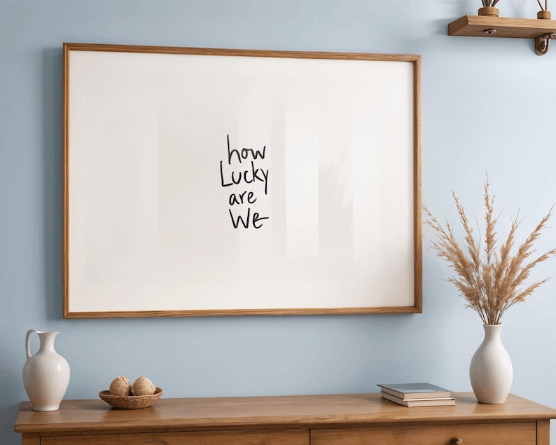 A minimalist wall art print featuring the quote “How Lucky Are We” in elegant hand-drawn typography on a neutral background. The modern canvas design exudes warmth and simplicity, perfect for couples who value love and gratitude. This inspirational quote poster adds a timeless touch to any contemporary or boho-style home. A beautifully crafted neutral wall decor piece that symbolizes appreciation, connection, and modern elegance.