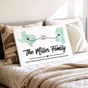 Op de afbeelding: Witte canvas print met een kaart van twee staten verbonden door een hartvormige lijn. De tekst "The Miller Family" is in sierlijke letters geschreven, met de zin "Family Forever Never Apart. Maybe in Distance But Never in Heart" eronder.