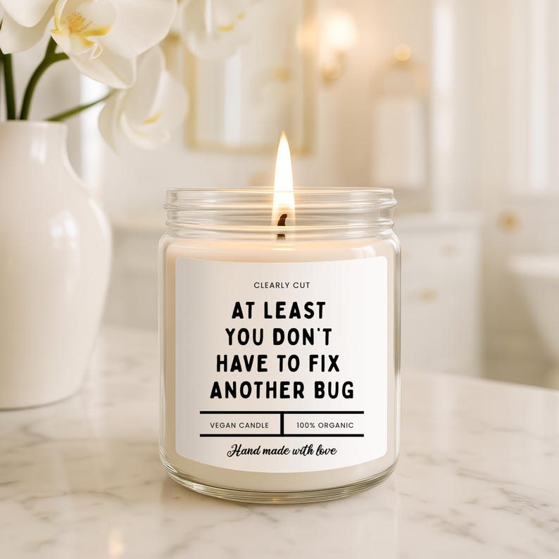 Peut inclure: Une bougie en pot de verre transparent avec une m&egrave;che allum&eacute;e et une &eacute;tiquette blanche portant le texte : CLEARLY CUT, AT LEAST YOU DON'T HAVE TO FIX ANOTHER BUG, VEGAN CANDLE, 100% ORGANIC, et Hand made with love. La cire est blanc cass&eacute;.