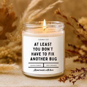 Peut inclure: Une bougie en pot de verre transparent avec une m&egrave;che allum&eacute;e et une &eacute;tiquette blanche portant le texte noir : CLEARLY CUT, AT LEAST YOU DON'T HAVE TO FIX ANOTHER BUG, VEGAN CANDLE, 100% ORGANIC, et Hand made with love. La cire est blanc cass&eacute;.
