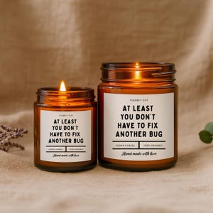 Peut inclure: Deux bougies en pot en verre ambr&eacute; avec des m&egrave;ches allum&eacute;es. Chaque &eacute;tiquette blanche porte le texte : CLEARLY CUT, AT LEAST YOU DON'T HAVE TO FIX ANOTHER BUG, VEGAN CANDLE, 100% ORGANIC, et Hand made with love. Les bougies sont de tailles diff&eacute;rentes.