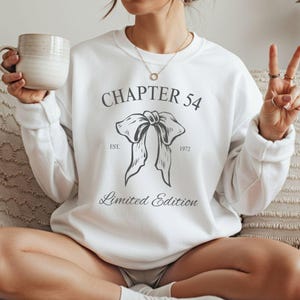 May include: White sweatshirt with the text "CHAPTER 54" above a bow illustration. Below the bow, the text reads "Limited Edition" and "EST. 1972". The sweatshirt is a crew neck style.