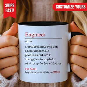 Puede incluir: Una taza de cerámica blanca con interior y asa negros. El frente presenta texto negro que define la palabra Engineer como un profesional que resuelve problemas imposibles, con el texto rojo See Also: logical, innovative, JAMES.
