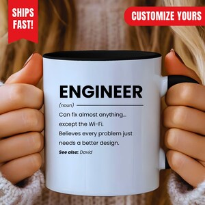 Op de afbeelding: Een witte keramische mok met een zwarte binnenkant en handvat, voorzien van de zwarte tekst: ENGINEER (noun) Can fix almost anything... except the Wi-Fi. Believes every problem just needs a better design. See also: David.