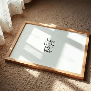 A minimalist wall art print featuring the quote “How Lucky Are We” in elegant hand-drawn typography on a neutral background. The modern canvas design exudes warmth and simplicity, perfect for couples who value love and gratitude. This inspirational quote poster adds a timeless touch to any contemporary or boho-style home. A beautifully crafted neutral wall decor piece that symbolizes appreciation, connection, and modern elegance.