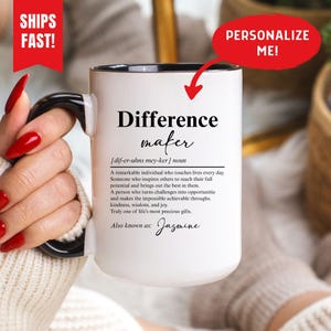 Può includere: Una tazza in ceramica bianca con manico e interno neri. La parte anteriore presenta un testo nero che definisce il termine Difference maker, seguito da un paragrafo descrittivo e dal nome Jasmine. Il design include la trascrizione fonetica.