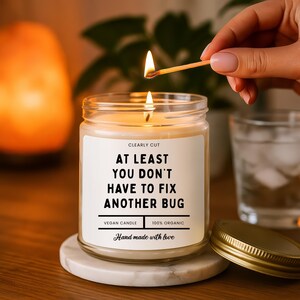 Peut inclure: Une bougie en pot de verre transparent avec une &eacute;tiquette blanche portant le texte noir : CLEARLY CUT, AT LEAST YOU DON'T HAVE TO FIX ANOTHER BUG, VEGAN CANDLE, 100% ORGANIC, Hand made with love. La bougie a une m&egrave;che allum&eacute;e et un couvercle dor&eacute;.