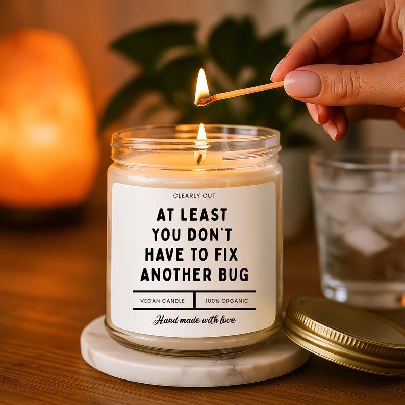Peut inclure: Une bougie en pot de verre transparent avec une &eacute;tiquette blanche portant le texte noir : CLEARLY CUT, AT LEAST YOU DON'T HAVE TO FIX ANOTHER BUG, VEGAN CANDLE, 100% ORGANIC, Hand made with love. La bougie a une m&egrave;che allum&eacute;e et un couvercle dor&eacute;.
