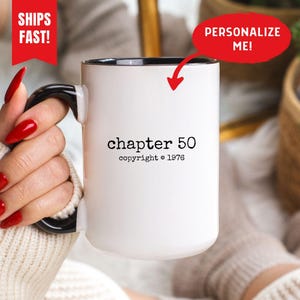以下が含まれることがあります： 黒いハンドルと縁が付いた白いセラミックマグ。マグには、黒で「chapter 50 copyright © 1976」というテキストが記載されています。赤いバナーには「PERSONALIZE ME！」と書かれています。