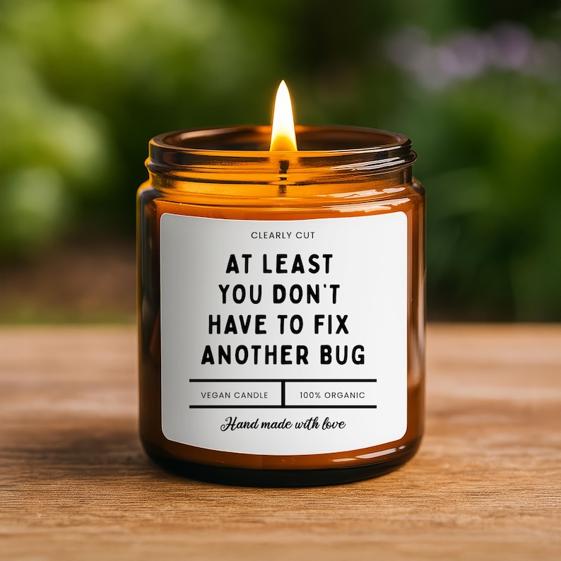 Peut inclure: Une bougie allum&eacute;e dans un pot en verre ambr&eacute; avec une &eacute;tiquette blanche portant le texte : CLEARLY CUT, AT LEAST YOU DON'T HAVE TO FIX ANOTHER BUG, VEGAN CANDLE, 100% ORGANIC, et Hand made with love. La bougie a une m&egrave;che allum&eacute;e.