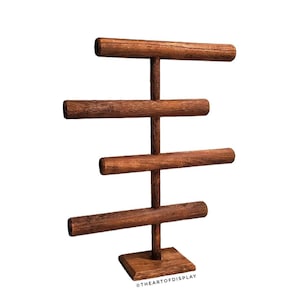 May include: A wooden jewelry display stand with four horizontal bars for displaying bracelets or necklaces. The stand is made of dark brown wood and has a square base. The text "@THEARTOFDISPLAY" is visible on the base.