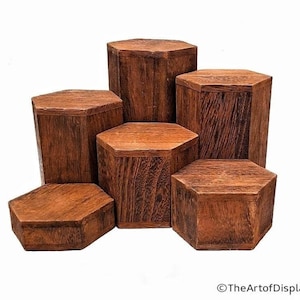May include: A collection of six hexagonal wooden display stands in varying heights. The stands are made of dark brown wood with visible grain patterns. The arrangement suggests a tiered display setup, suitable for showcasing products.