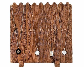May include: Wooden necklace display stand with five gold chains and pendants. The stand has a scalloped top edge and is on two small legs. The text "THE ART OF DISPLAY" is visible on the stand.