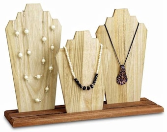 May include: Three wooden necklace display stands with necklaces. The stands are light-colored wood with a dark wood base. The necklaces include pearls, black beads, and a pendant.