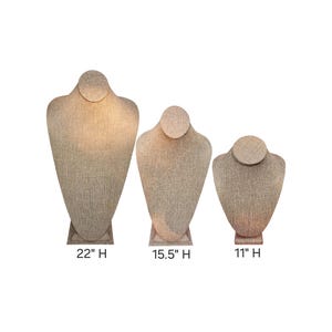 May include: Three beige linen necklace display busts in varying sizes: 22 inches, 15.5 inches, and 11 inches high. Each bust has a rounded neck and a rectangular base. The fabric has a textured appearance, suitable for showcasing jewelry.