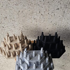 May include: Three tiered jewelry displays in beige, black, and gray. Each display has multiple levels with cone-shaped holders for rings or other jewelry. The displays are on a white stool against a textured wall.