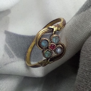 Puede incluir: Un anillo de oro con un diseño de flor con piedras preciosas azules y rosas.