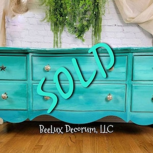 May include: A turquoise dresser with six drawers and a curved front. The dresser has a distressed finish and features star-shaped drawer pulls. The dresser is sold and the text "SOLD" is superimposed on the image. The text "Beelux Decor, LLC" is at the bottom of the image.