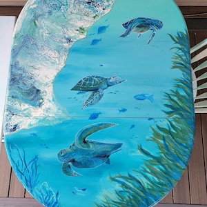 May include: A round, blue and green table top with a painted ocean scene. The scene features three sea turtles swimming in the water with seaweed and fish.