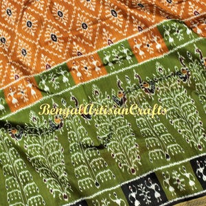 May include: A detailed shot of a textile with a vibrant pattern. The fabric features a repeating design in shades of orange, green, and white. The text "Bengal Artisan Crafts" is visible on the fabric.