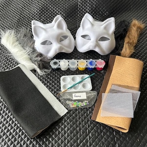 May include: A craft kit with two white cat masks, paint, brushes, felt, faux fur, and gems. The kit includes a variety of colors and textures for creating custom masks. Perfect for DIY projects and creative activities.