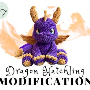 May include: A handmade purple crochet dragon with gold accents, including wings, horns, and feet. The dragon has large, expressive eyes and is sitting. The image includes the text "Dragon Hatchling MODIFICATION" in a decorative font.