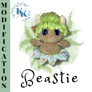 May include: A crocheted plush toy with green hair, brown fur, blue eyes, and a light blue and pink skirt. The toy is sitting on a green background with the word "Beastie" written in cursive below it.