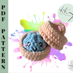 May include: A crochet PDF pattern featuring a light blue plush dumpling with a smiling face and pink cheeks, nestled inside a peach-coloured crocheted steamer basket with a matching lid. The text PDF PATTERN is printed vertically on the left side.