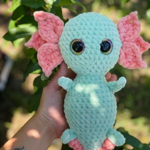May include: A crocheted axolotl plush toy with pink fins and large, glittery eyes. The toy is light green and has a soft, fuzzy texture.