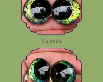Puede incluir: Dos pares de ojos de cristal con temática de Raptor. Los ojos tienen una pupila negra y un iris multicolor con tonos verdes, amarillos y azules. El texto "Raptor" está debajo del par de ojos superior.