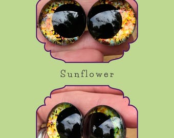 Puede incluir: Dos ojos redondos de vidrio negro con un diseño inspirado en el girasol. Los ojos tienen un acabado iridiscente dorado, naranja y verde.