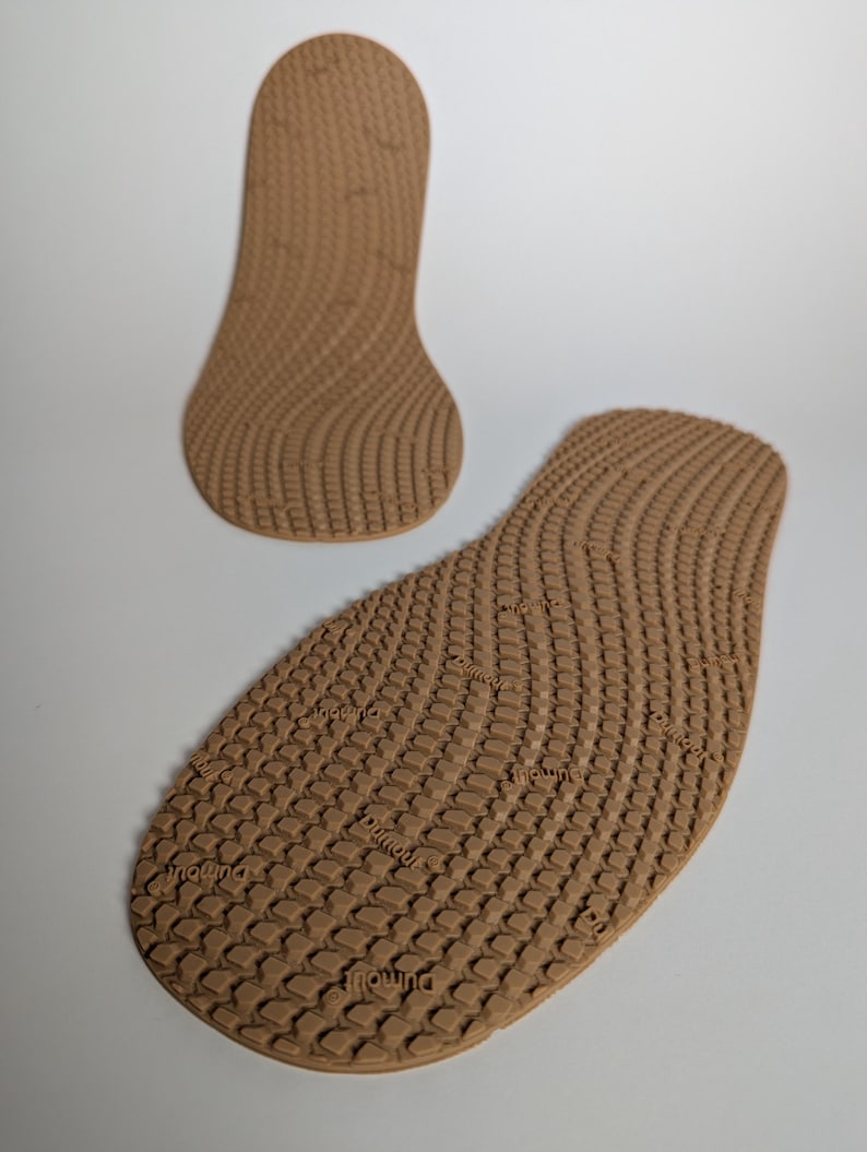 May include: Two brown shoe insoles with a textured, wave-like pattern. One insole is in the shape of the entire foot, and the other is the shape of the heel. The insoles have the word "dumoulin" printed on them.