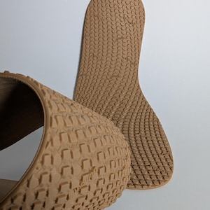 May include: Tan-colored shoe insoles with a textured pattern. One insole is curved, and the other is flat, both with a repeating geometric design. The insoles are made of a flexible material.