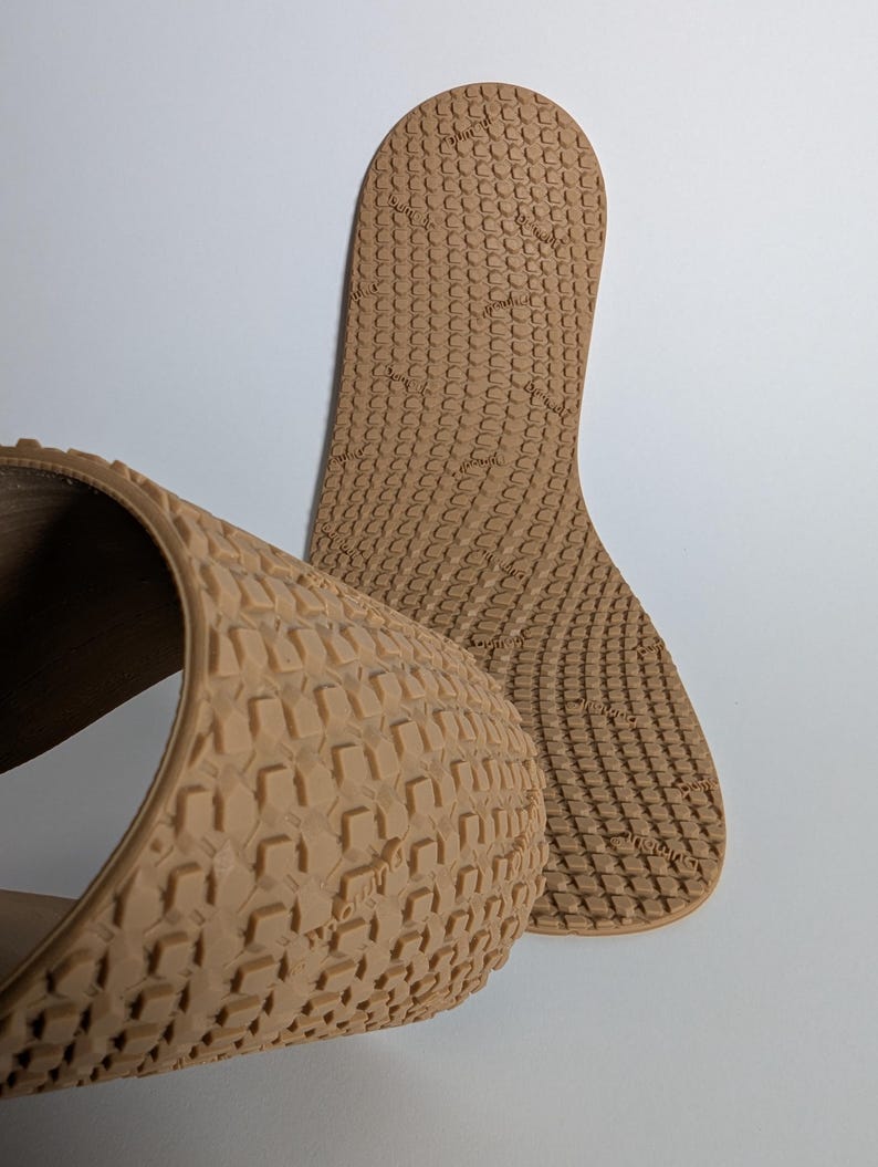 May include: Tan-colored shoe insoles with a textured pattern. One insole is curved, and the other is flat, both with a repeating geometric design. The insoles are made of a flexible material.
