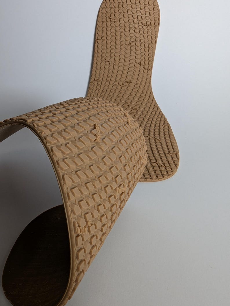 May include: Tan-colored shoe insoles with a textured, repeating pattern. The insoles are flexible and curved, with one insole partially folded over. The design includes the text "Dunk" on the insole.