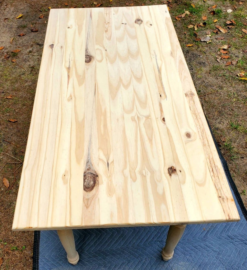 Pu&ograve; includere: Un piano da tavolo in legno chiaro con finitura a venatura naturale. Il tavolo ha gambe tornite ed &egrave; appoggiato su un telo blu.