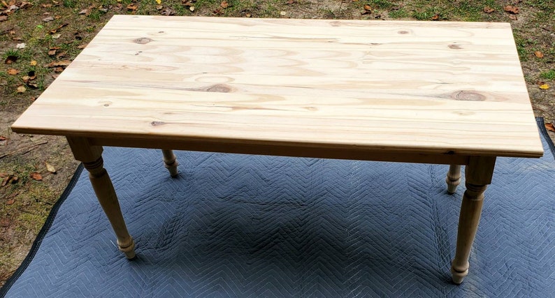 Pu&ograve; includere: Un tavolo in legno chiaro con un piano rettangolare e gambe tornite. Il tavolo &egrave; appoggiato su un tappeto a motivi neri e grigi.