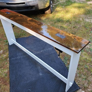 May include: White wooden table with a dark brown stained top. The table has a built-in power strip with multiple outlets.
