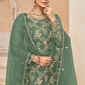 Op de afbeelding: Een groene geborduurde jurk met een bijpassende dupatta. De jurk heeft een bloemenpatroon en een ronde halslijn. De dupatta is doorschijnend en heeft een kantversiering. De jurk wordt getoond op een model met een gouden ketting en oorbellen. D.NO.: 7702
