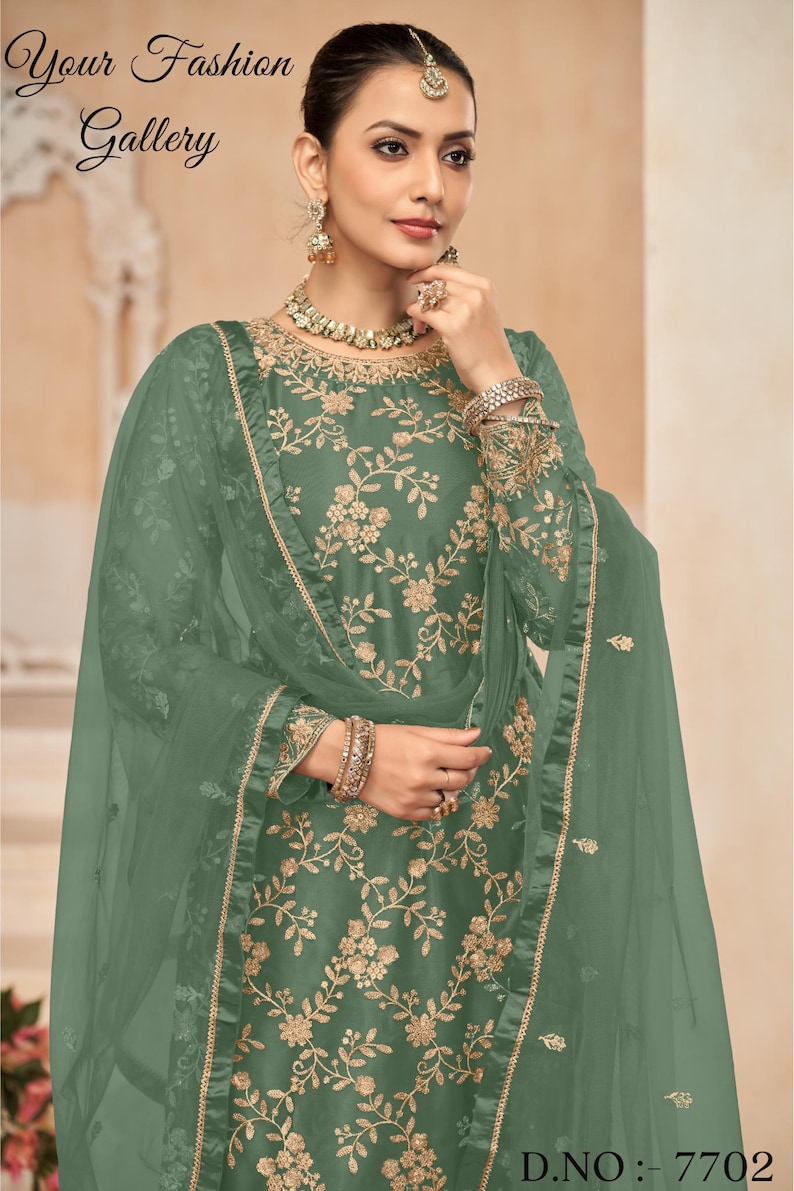 Op de afbeelding: Een groene geborduurde jurk met een bijpassende dupatta. De jurk heeft een bloemenpatroon en een ronde halslijn. De dupatta is doorschijnend en heeft een kantversiering. De jurk wordt getoond op een model met een gouden ketting en oorbellen. D.NO.: 7702